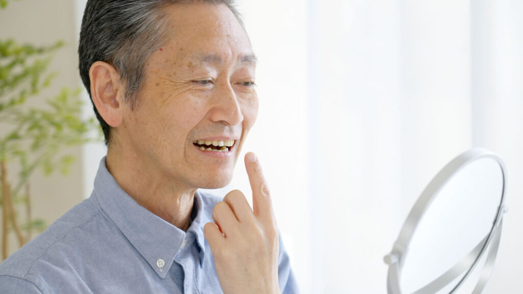 歯で鏡を見ながら笑う高齢男性