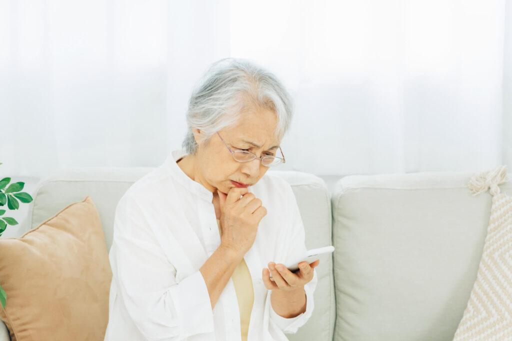 スマホを見ながら悩む高齢女性