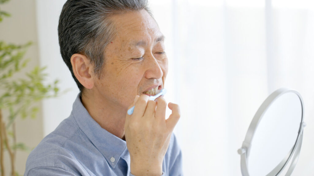 鏡を見ながら歯磨きをする高齢男性