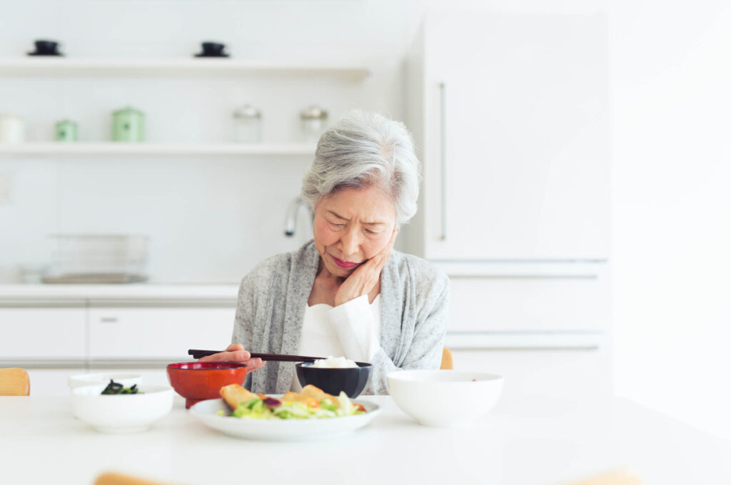 食卓を前に歯を押さえる高齢女性