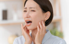 顎を押さえて口を開け、痛そうな表情を浮かべる人